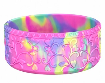 May include: A circular silicone boot featuring a vibrant tie-dye pattern of pink, yellow, purple, and teal. The exterior is embossed with a repeating heart-shaped vine motif and a border of small hearts along the top edge of the cylindrical band.