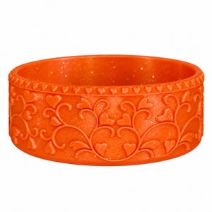 May include: A bright orange bangle bracelet featuring a glittery finish and a raised relief pattern of swirling vines and small hearts. The top edge of the circular bracelet is decorated with a continuous border of tiny embossed heart shapes.