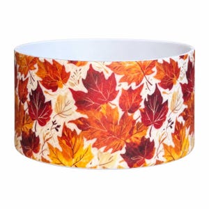 May include: A cylindrical bowl featuring a repeating pattern of autumn maple leaves in shades of vibrant orange, deep red, and golden yellow against a cream-colored background. The interior of the bowl is a solid, smooth white finish.