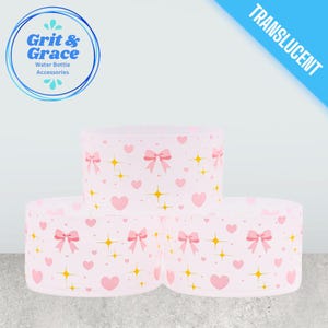 Può includere: Tre accessori traslucidi per bottiglie d'acqua con un motivo a fiocco rosa, cuore e stella. Gli accessori sono cilindrici e impilati. L'angolo in alto a sinistra presenta un logo con la scritta "Grit & Grace Water Bottle Accessories".