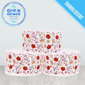 Può includere: Tre accessori per bottiglie d'acqua con sfondo bianco e un motivo ripetuto di mele rosse, matite, fiori e libri. Gli accessori hanno il testo "Grit & Grace Water Bottle Accessories" in un cerchio blu e la parola "TRANSLUCENT" in uno striscione blu.