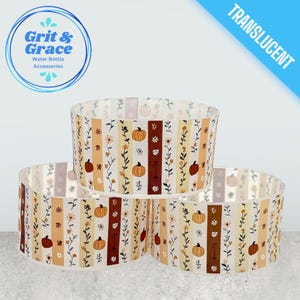 Può includere: Tre accessori traslucidi per bottiglie d'acqua con un motivo a righe verticali. Il design include zucche, fiori e foglie nei toni dell'arancione, del marrone e del crema. Il marchio "Grit & Grace" è visibile.