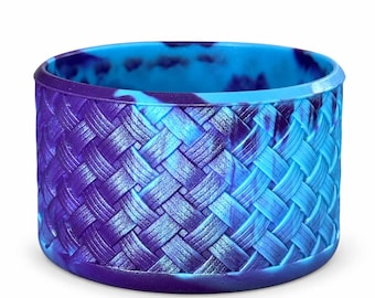 May include: A cylindrical silicone boot featuring a textured, woven basket-weave pattern. The surface displays a marbled color gradient transitioning from deep purple to vibrant sky blue, with a smooth, solid-colored rim at the top and bottom edges.