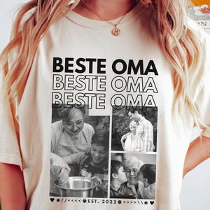 Puede incluir: Camiseta color crema con la frase "BESTE OMA" repetida tres veces, y un collage de fotos en blanco y negro. Las fotos muestran a una abuela con miembros de su familia. La camiseta tambi&eacute;n incluye el texto "EST. 2022" y s&iacute;mbolos de coraz&oacute;n.