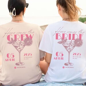 Könnte beinhalten: Zwei T-Shirts mit einem Cocktail-Motiv. Eines ist beige mit "Here comes the CREW" und das andere ist weiß mit "Here comes the BRIDE". Beide Shirts tragen das Datum "05 APRIL 2025" und den Text "BACHELORETTE".