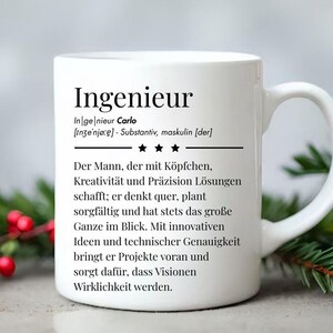 Könnte beinhalten: Weiße Keramik-Tasse mit dem deutschen Wort "Ingenieur" in Schwarz bedruckt. Die Tasse hat eine Definition und Beschreibung unter dem Wort. Die Tasse steht auf einer Oberfläche mit roten Beeren und grünem Laub.