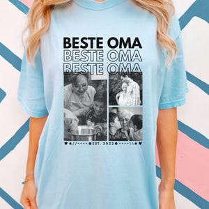 Puede incluir: Camiseta azul claro con el texto "BESTE OMA" repetido tres veces en negro. La camiseta presenta un collage de fotos en blanco y negro y el texto "EST. 2022".