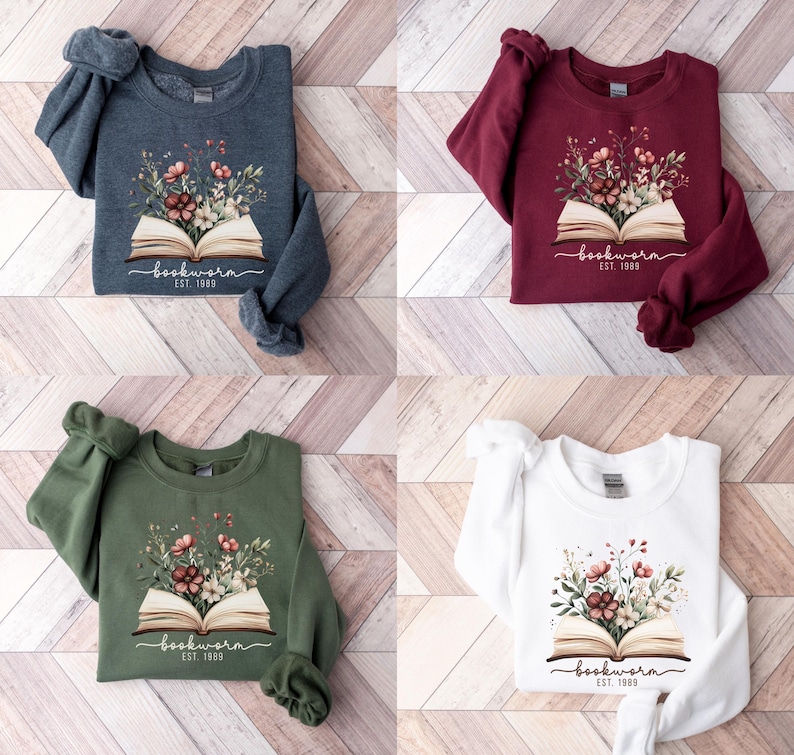May include: Four sweatshirts in navy, burgundy, olive green, and white. Each has a floral design sprouting from an open book, with the word "bookworm" and "EST. 1989" printed below. A cozy, casual style.
