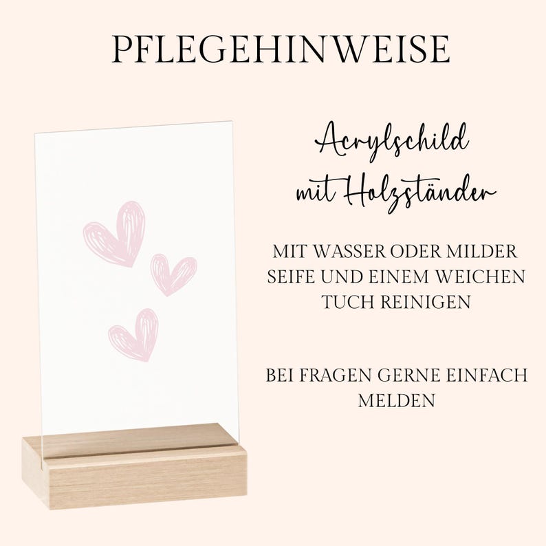 May include: A clear acrylic sign with three pink heart illustrations, set in a natural wood base. The sign includes German text: "PFLEGEHINWEISE" and "Acrylschild mit Holzst&auml;nder". Instructions for cleaning are also included.