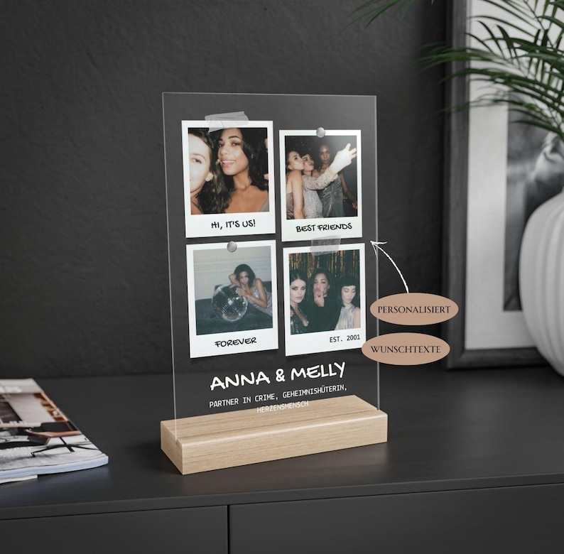 May include: A clear acrylic photo display with four attached photos. The photos are held in place with silver push pins. The display sits on a light wood base. Text on the display reads "Hi, it's us!", "Best Friends", "Forever", "Anna & Melly", and "Est. 2001".