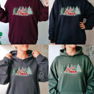 May include: A collection of four long-sleeve hooded sweatshirts in maroon, black, dark gray, and forest green. Each hoodie features a central graphic print of a red car carrying a pine tree in front of red buildings and snow-covered pine trees.