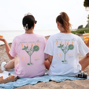 May include: Two people wearing white and pink t-shirts with a cocktail graphic and the text "Here comes the bride" and "Here comes the crew".