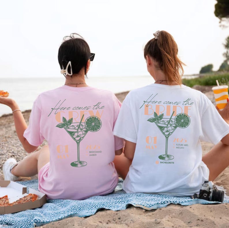 May include: Two people wearing white and pink t-shirts with a cocktail graphic and the text "Here comes the bride" and "Here comes the crew".