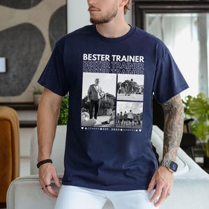 May include: Navy blue t-shirt featuring the text "BESTER TRAINER" above a collage of black and white photos. The photos show a person and a group of people. The shirt has a crew neck and is made of cotton.