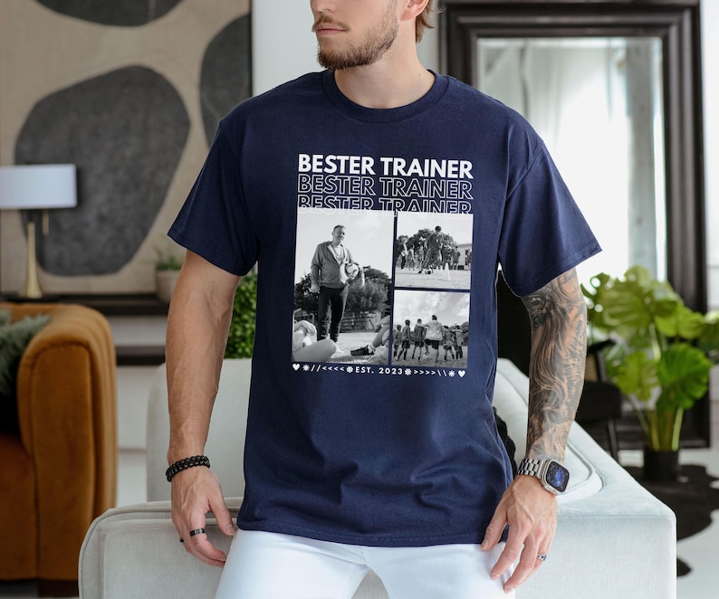 May include: Navy blue t-shirt featuring the text "BESTER TRAINER" above a collage of black and white photos. The photos show a person and a group of people. The shirt has a crew neck and is made of cotton.