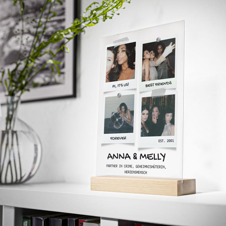 May include: A clear acrylic photo display with four instant photos attached. The photos feature groups of women. The display has a wooden base and text that reads "ANNA & MELLY" and "PARTNER IN CRIME, GEHEIMNISH&Uuml;TERIN, HERZENSMENSCH."