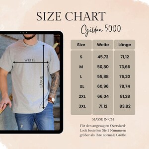 May include: A size chart for Gildan 5000 t-shirts, with measurements in centimetres. Sizes range from S to 3XL. The image shows a person in a grey t-shirt and jeans, with a table detailing chest and length measurements.