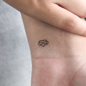 Può includere: Un piccolo tatuaggio a forma di simbolo di infinito con un cuore al centro, sul polso di una persona.