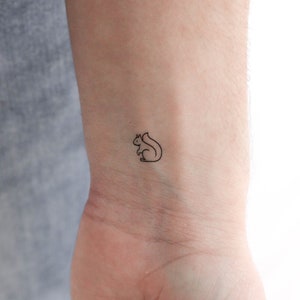 Puede incluir: Un dibujo simple de línea de una ardilla, tatuado en la muñeca de una persona.