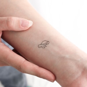 May include: A simple line drawing of a turtle on a person's wrist. The tattoo is small and delicate.
