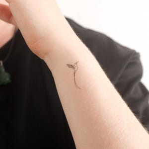 Op de afbeelding: Een eenvoudige lijntekening tattoo van een kolibrie op de pols van een persoon.