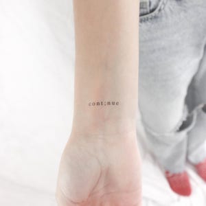 Könnte beinhalten: Nahaufnahme eines Handgelenks mit einem kleinen Tattoo, auf dem "cont;nue" steht.