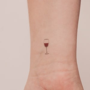 Könnte beinhalten: Eine einfache Tattoo-Zeichnung eines Weinglases mit Rotwein darin.