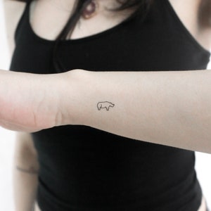 May include: A simple line drawing tattoo of a rhinoceros on a person's wrist.