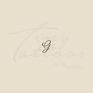 May include: A black, cursive letter "G" temporary tattoo. The tattoo is 0.5 inches (1.3 cm) in height. The background is a light beige color with the words "Tiny Tattoos" and "by tatteco" in a faded, cursive font.