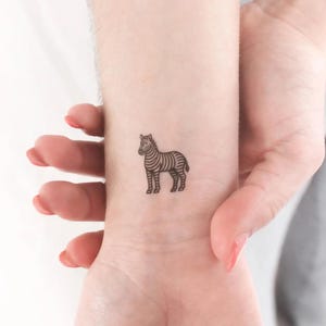 Puede incluir: Un pequeño tatuaje de cebra en blanco y negro en la muñeca de una persona.