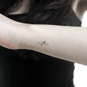 May include: A simple black infinity symbol tattoo with an arrow going through it.