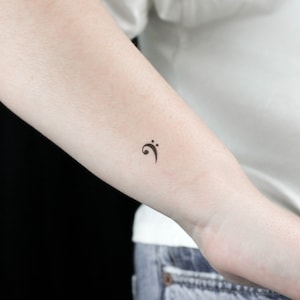 Op de afbeelding: Een kleine zwarte basissleutel tattoo op de onderarm van een persoon.