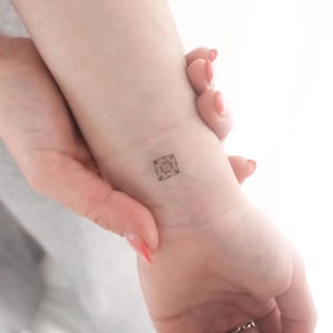 May include: A small, intricate, black and white geometric design tattoo on a person's wrist.