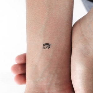 May include: A black and white temporary tattoo of the Eye of Horus, an ancient Egyptian symbol.
