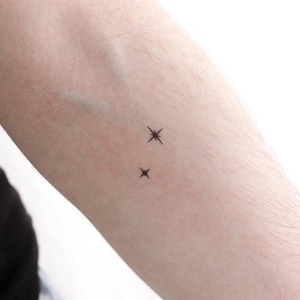 Peut inclure: Gros plan sur le bras d'une personne avec deux petits tatouages d'étoiles.