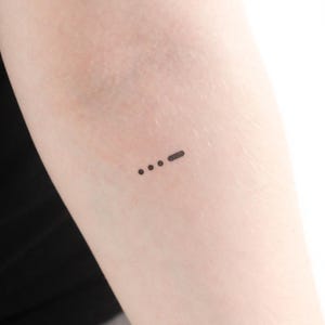 May include: A small tattoo of three dots and a dash on a person's arm. This is a common tattoo design that represents Morse code for the letter 'S'.