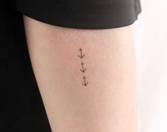 May include: A close-up of a person's arm with a small tattoo of four anchors in a vertical line.