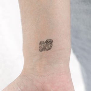 May include: A small, black and white dog tattoo on a person's wrist.
