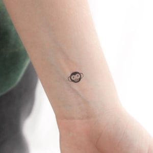 Könnte beinhalten: Ein kleines schwarz-weißes Affengesicht-Tattoo auf dem Handgelenk einer Person.