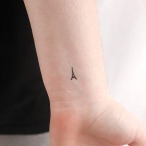 Puede incluir: Un pequeño tatuaje temporal negro de la Torre Eiffel en la muñeca de una persona.
