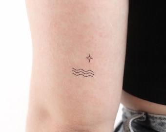 May include: A simple line art tattoo design of a star above a wavy line, representing water. The tattoo is on a person's arm.