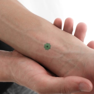 May include: A small green flower tattoo on a person's wrist.