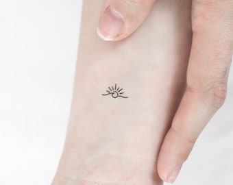 May include: A simple line drawing tattoo of a sun rising over a wave.