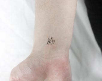 Peut inclure: Un tatouage simple en forme de ligne d'une colombe en vol sur le poignet d'une personne.