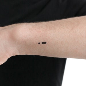 May include: A black semicolon tattoo on a person's wrist.