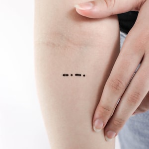 Könnte beinhalten: Ein kleines Tattoo mit drei Punkten auf dem Arm einer Person. Die Punkte sind in einer Reihe angeordnet, mit zwei Punkten links und einem Punkt rechts.
