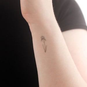 May include: A simple line drawing tattoo of an iris flower on a person's wrist.