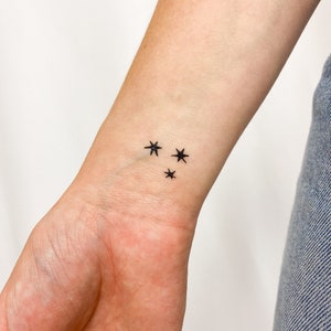 Può includere: Un primo piano di un polso con un piccolo tatuaggio nero di tre stelle.