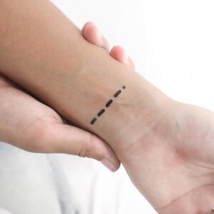 May include: A black tattoo of Morse code on a person's wrist.