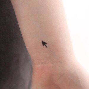 May include: A small black computer mouse cursor tattoo on a person's wrist.